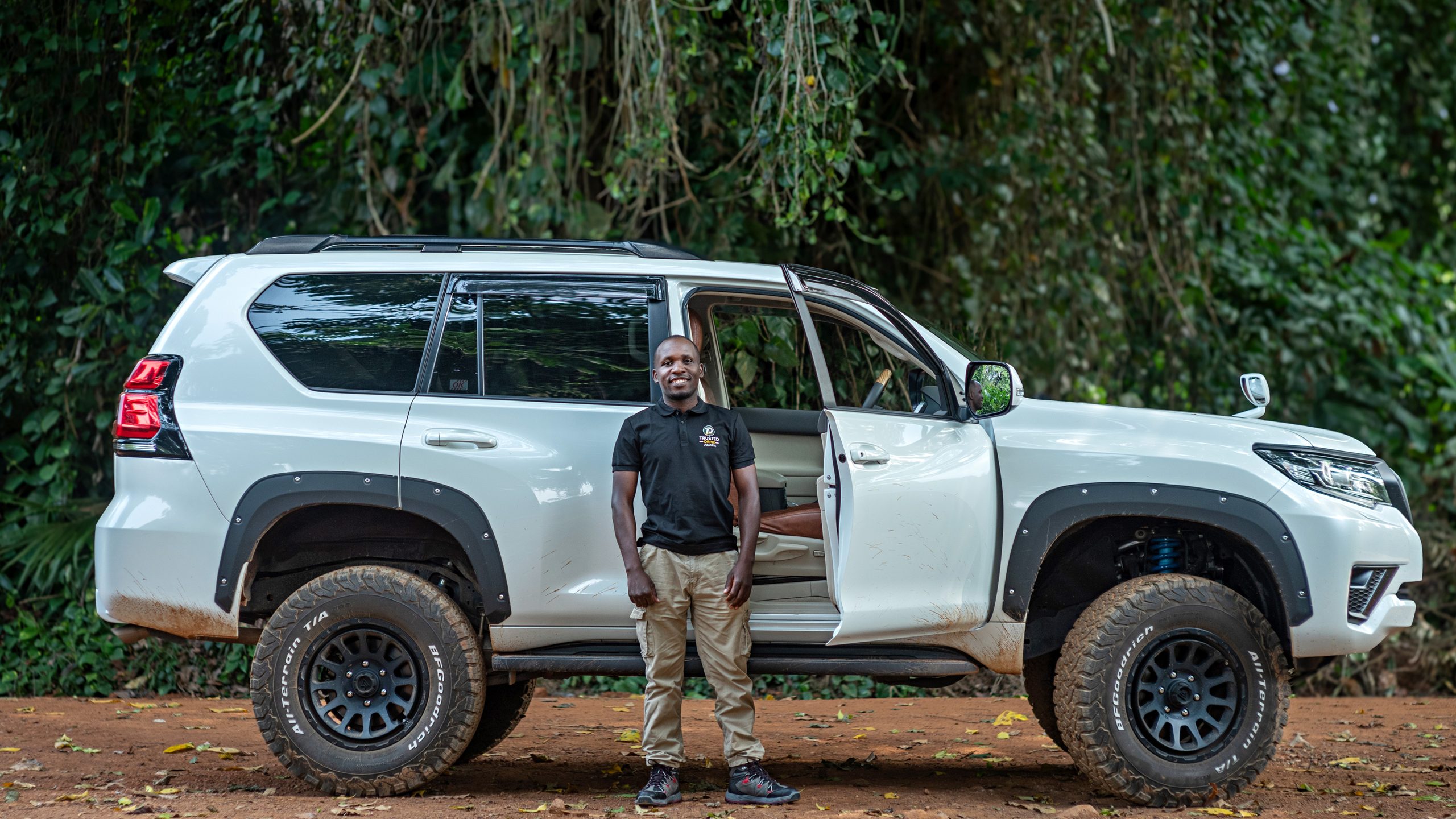 Trusted Drive driver standing beside a white Toyota Land Cruiser Prado